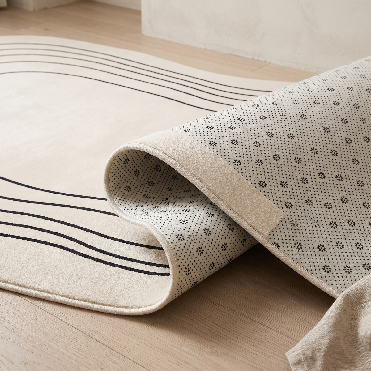 Corner of the Ovala rug folded back to reveal the pale anti-slip backing printed with a dense grid of dots and small florets