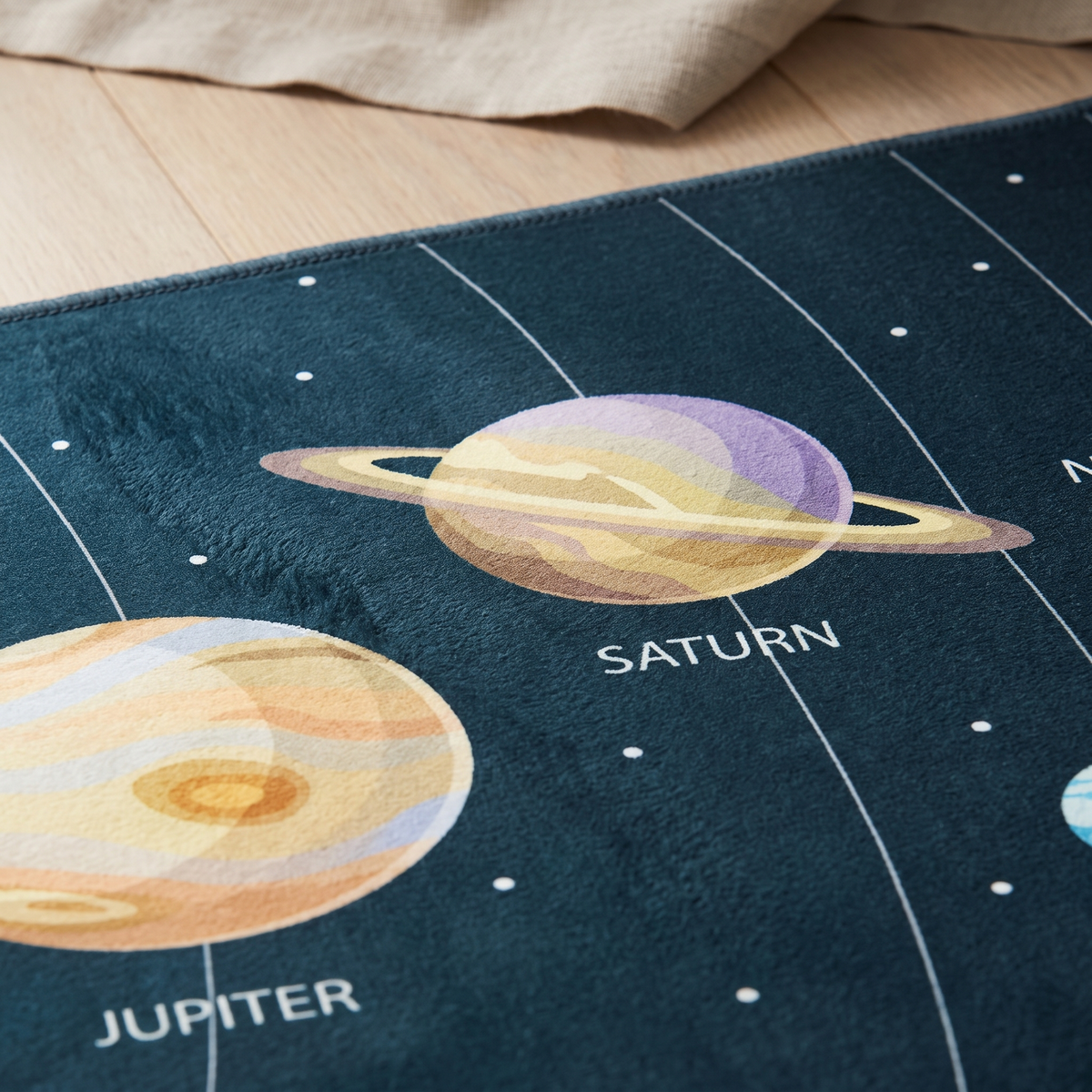 Close-up of the Orbit rug's short polyester pile and overlocked edge, showing the printed Saturn and Jupiter detail