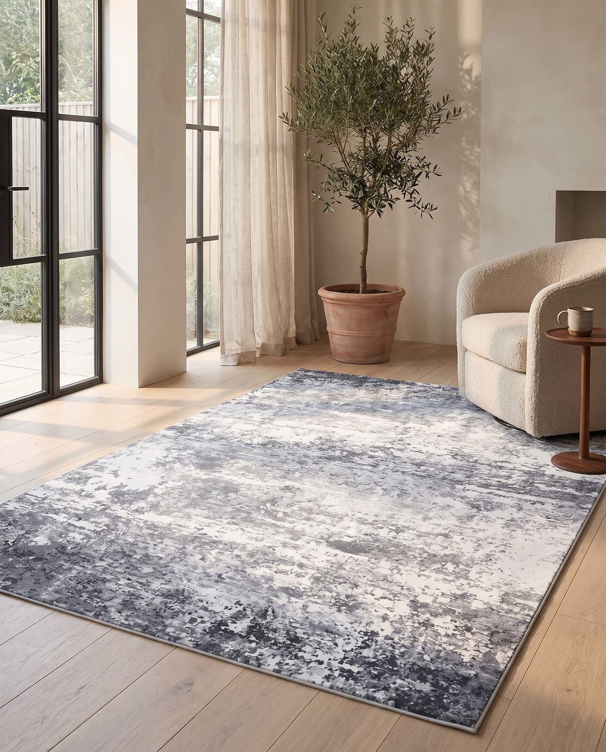 Marlo rug in a warm-neutral garden room with a boucle armchair, olive tree and crittall doors in afternoon light