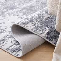 Corner of the Marlo rug folded back to show the low flat pile, the stitched edge and the woven grey non-slip polypropylene backing
