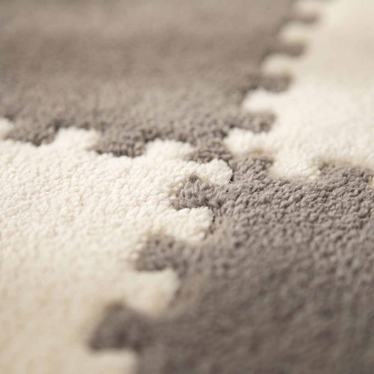 Macro close-up of the short dense plush pile where an ivory Tessa tile clips into a mid grey tile along the interlocking jigsaw seam