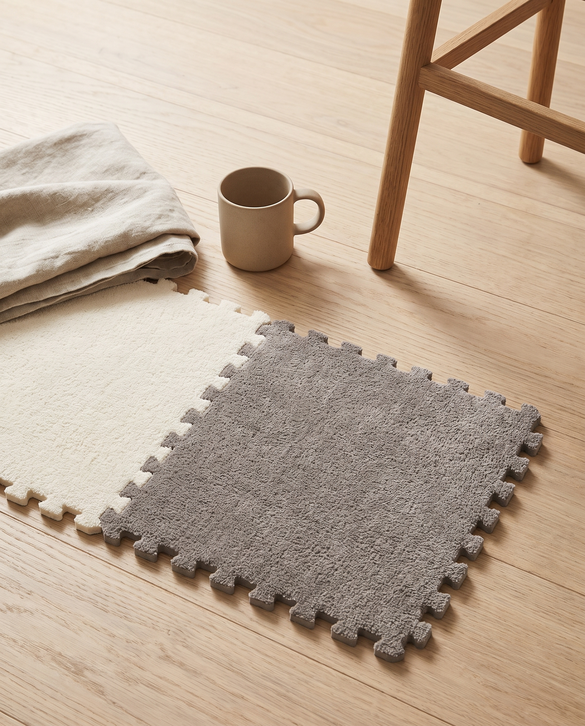 Two Tessa tiles clipped together on a pale oak floor beside a stoneware mug, folded linen throw and oak stool leg showing the real size of a 30 by 30 cm tile