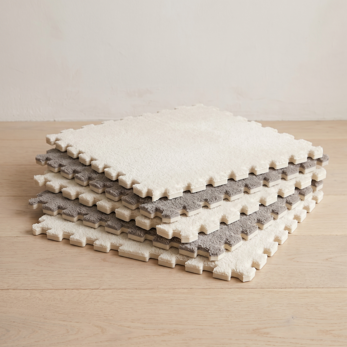 A low flat stack of individual Tessa tiles showing the plush top surface, the lightweight foam core and the interlocking teeth along each thin edge