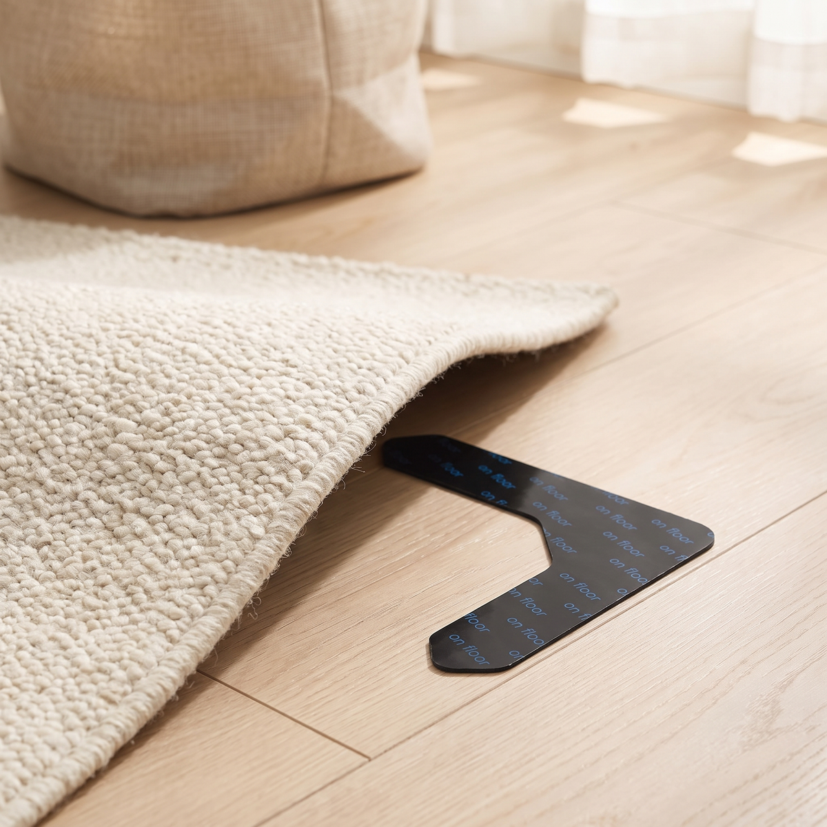 Corner of a cream wool rug folded back on oak flooring to reveal a fitted Gripo rug gripper