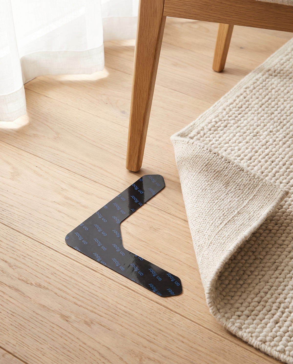 Gripo rug gripper on oak flooring beside a chair leg and rug corner showing its real size