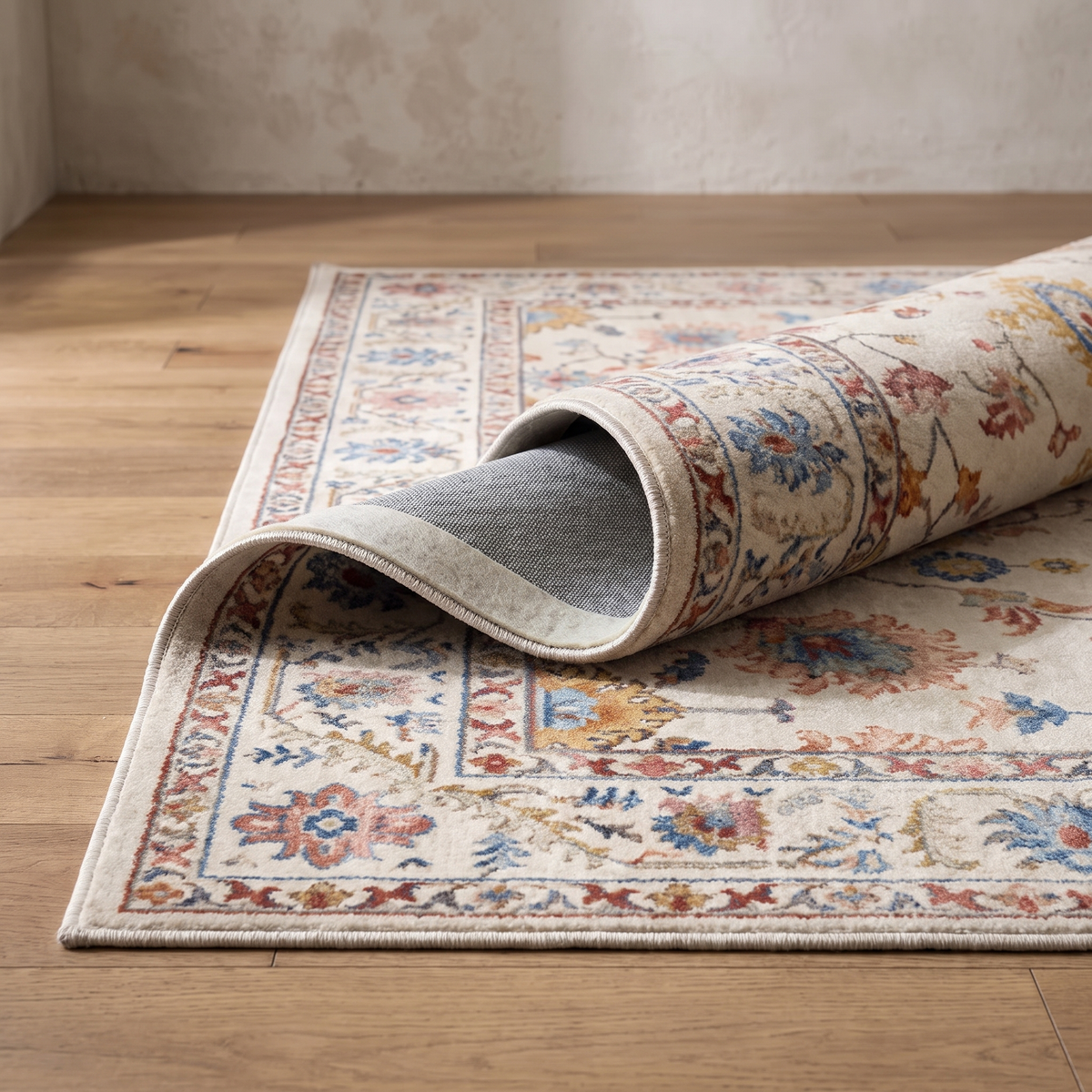 Corner of the Bahia rug curled back on an oak floor, showing the bound edge, the multi-band border and the felt underlayer over the PVC backing
