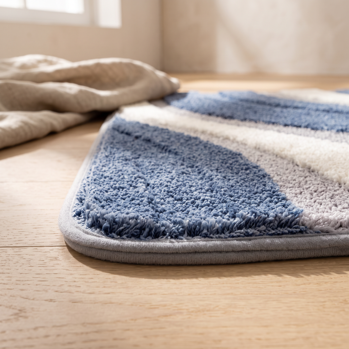 Detail of one rounded corner of the Nima bath mat at floor level, showing the depth of the pile and the narrow grey bound edge in profile