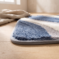 Detail of one rounded corner of the Nima bath mat at floor level, showing the depth of the pile and the narrow grey bound edge in profile