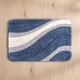 Nima bath mat seen from above on a pale oak floor, showing the full 50 x 80 cm rectangle, its sweeping indigo, ivory and dove grey arcs, rounded corners and grey bound edge