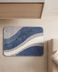 Overhead view of the Nima bath mat on a pale oak floor in front of a timber en-suite vanity, with a boucle stool and rolled linen towel at the edge of frame