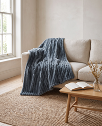Nordo grey throw blanket thrown over a natural linen sofa in a bright reading corner with a jute rug, oak coffee table and sash window