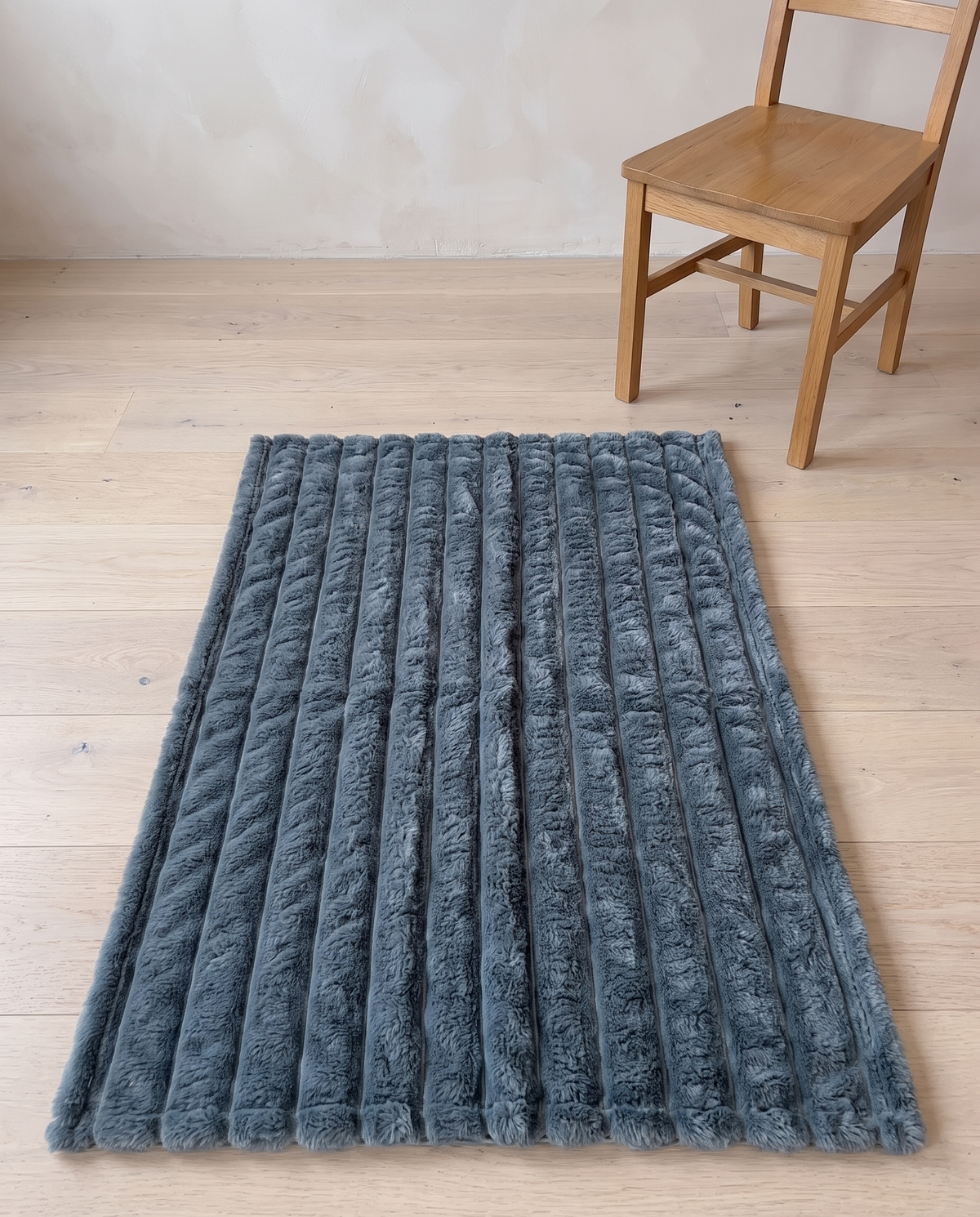 Nordo throw blanket laid flat on a pale oak floor beside an ordinary dining chair, giving a sense of its 100 by 150 cm size