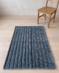 Nordo throw blanket laid flat on a pale oak floor beside an ordinary dining chair, giving a sense of its 100 by 150 cm size