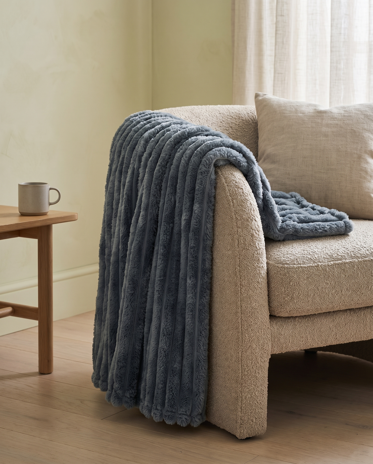Nordo grey throw blanket draped over the arm of an oatmeal boucle sofa in a calm sitting room with pale plaster walls and oak floorboards