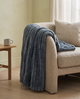 Nordo grey throw blanket draped over the arm of an oatmeal boucle sofa in a calm sitting room with pale plaster walls and oak floorboards