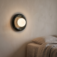 Avilo marble wall sconce lit beside a linen bed in a plaster walled bedroom