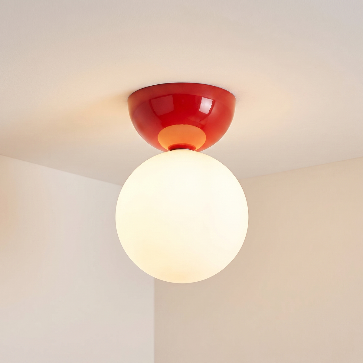 Close view of the red Vellona flush mount ceiling light against a plain white ceiling and cream wall