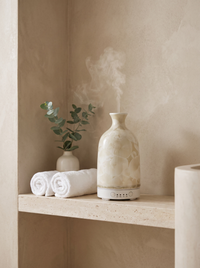 Aura Ceramic Stone Diffuser in Crystal Cream on a travertine bathroom shelf