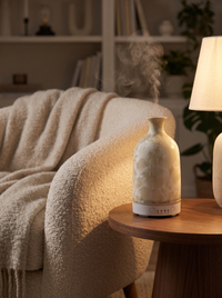 Aura Ceramic Stone Diffuser in Crystal Cream beside a boucle armchair at dusk