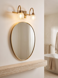 Prisa Prismatic Vanity Wall Light - lifestyle above oval mirror in warm cream bathroom with travertine shelf