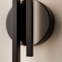 Eldra Disc Wall Light macro detail - twin matte black bars and circular disc backplate on cream wall