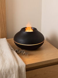 Volcano Flame Diffuser - lifestyle on oak bedside table with eucalyptus and linen, amber flame glowing