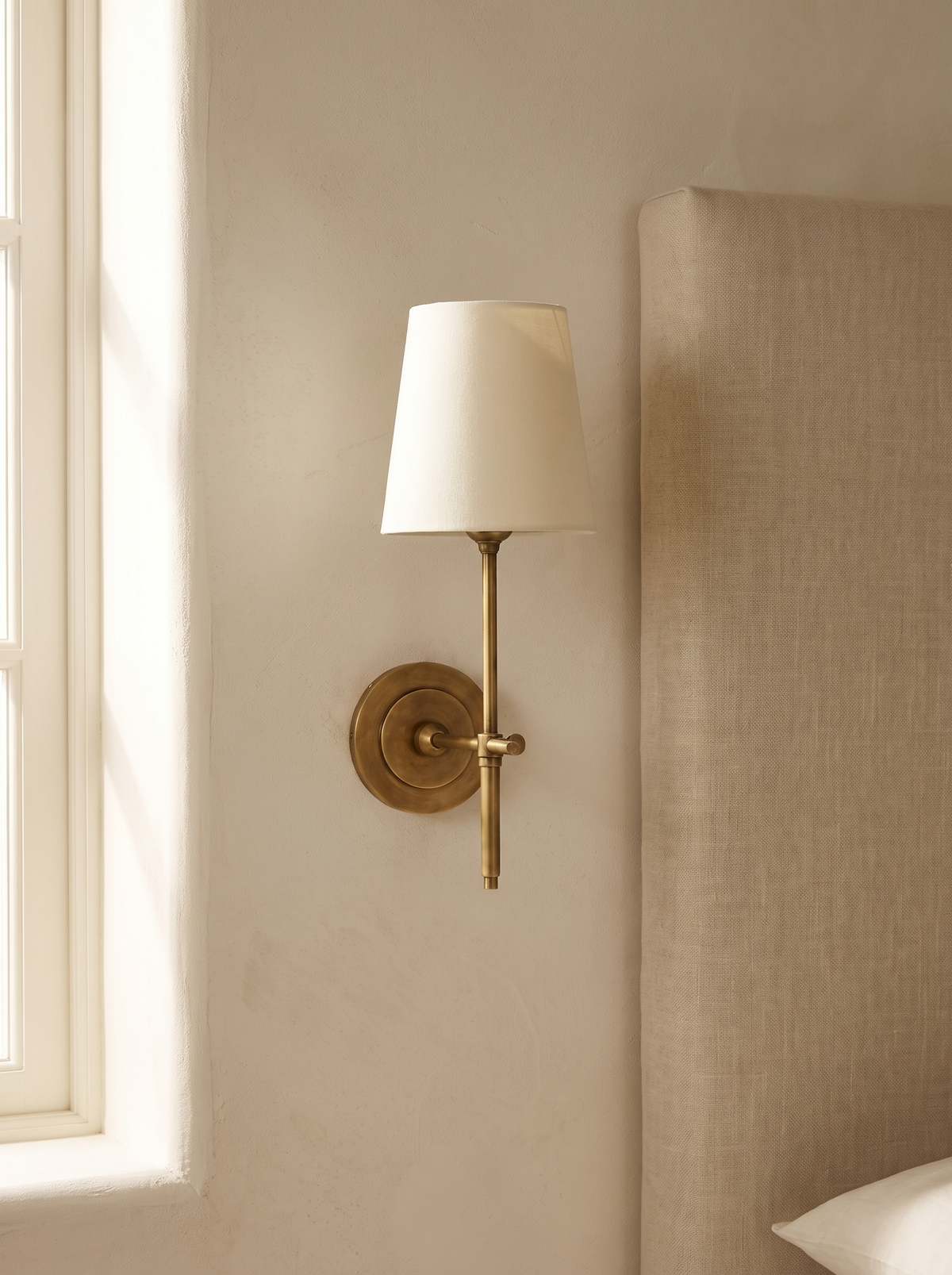 Thedo Brass Fabric Wall Light - scale context beside linen headboard in cream bedroom