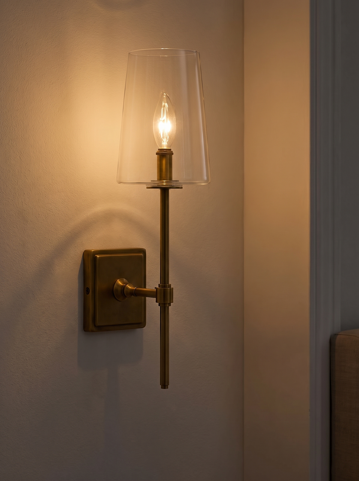 Torin Clear Glass Wall Sconce lit at dusk with warm amber 2700K candle glow