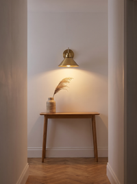 Arvo Bronze Cone Wall Light - warm glowing lifestyle in hallway with herringbone floor and console table