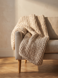 Cloud Chunky Knit Throw - draped over sofa arm in warm afternoon light with herringbone oak floor