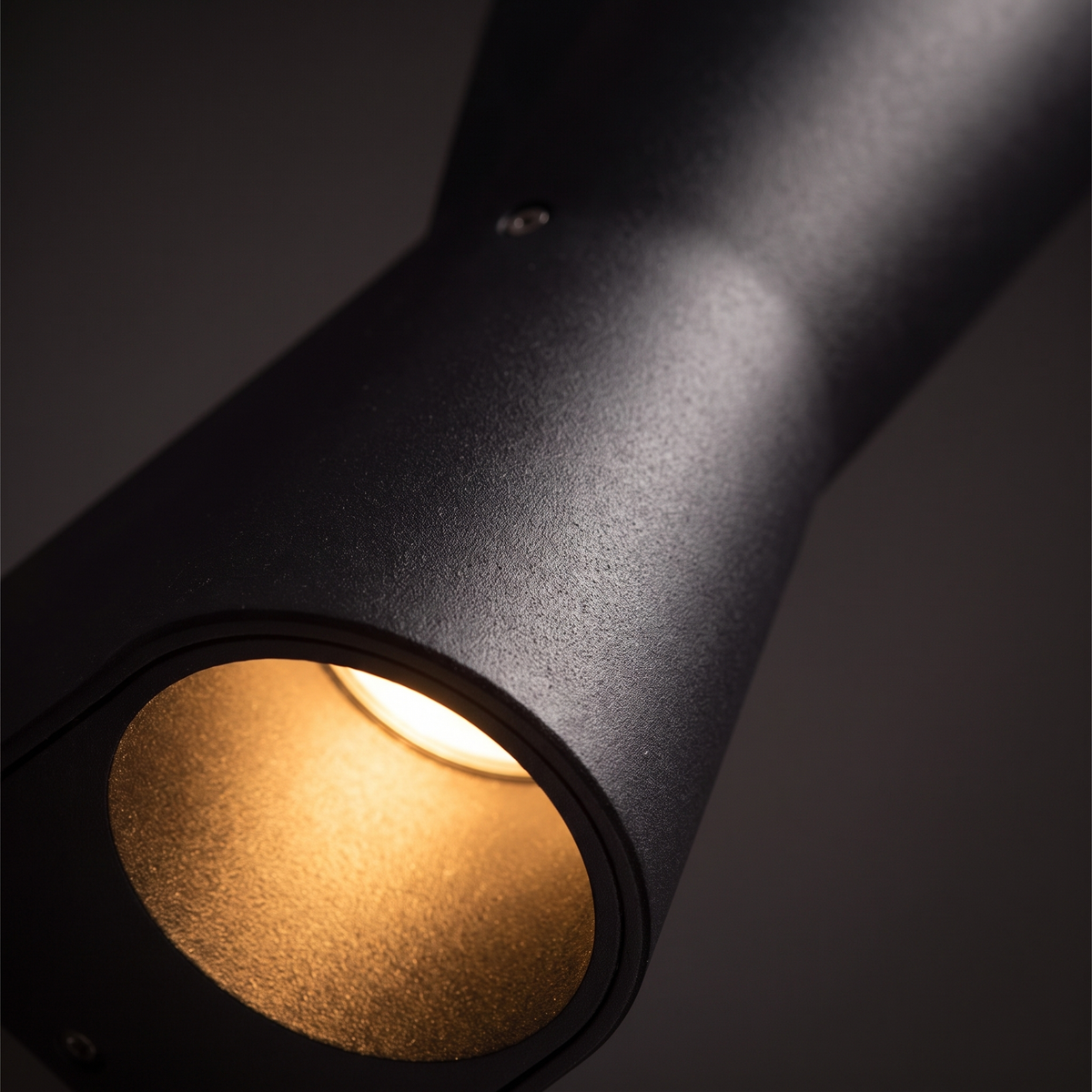 Kestro Torch Outdoor Wall Light - macro close-up of matte black powder-coat texture and warm LED glow from curved angled opening