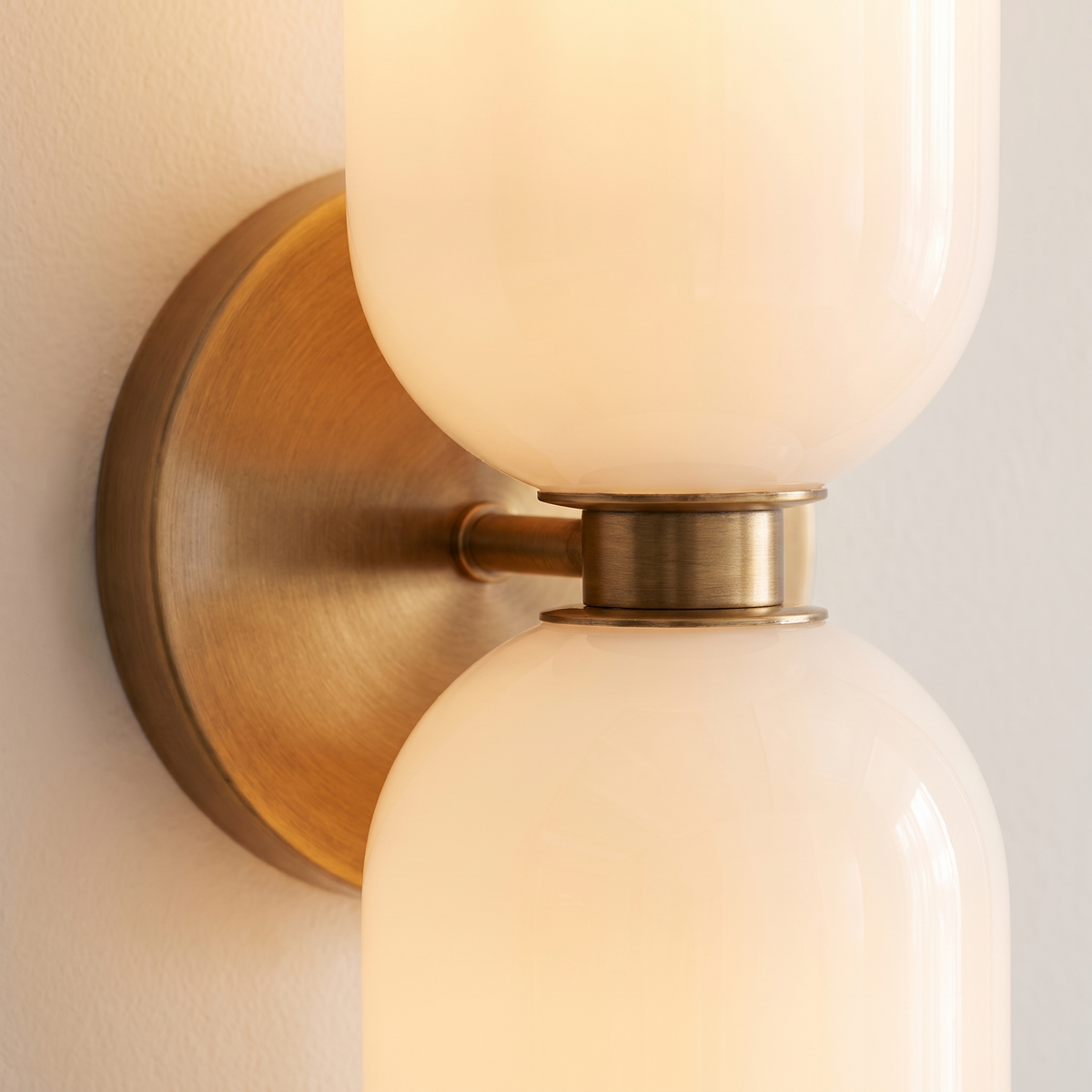 Solia Twin Glass Wall Sconce - macro close-up of opal glass shades and brushed brass disc junction showing warm translucent glow