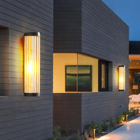 Yoro wall light lit on a grey brick house exterior at twilight, casting warm light up and down the wall