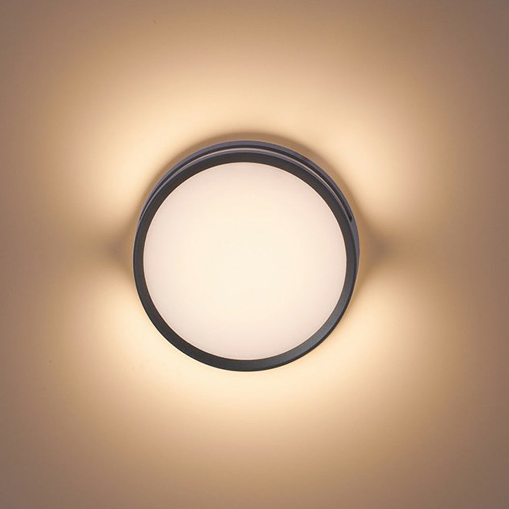 Vardo black outdoor wall light lit at close range, casting a warm halo across a pale wall