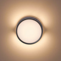 Vardo black outdoor wall light lit at close range, casting a warm halo across a pale wall