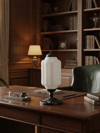 Elva glass table lamp lit on a wooden desk in a panelled study