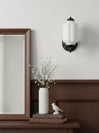 Elva milk glass wall sconce on a pale wall above a console and mirror